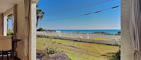 A covered patio with a view of the ocean, a white fence, and a grassy area.