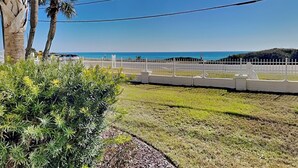 A coastal view with a white fence, palm trees, and a clear sky. - Lion On The Beach by Resort Collection (Panama City Beach)