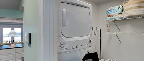 A modern laundry room with a large washer and dryer, a window with a view, and a shelf with a Hello Summer sign.