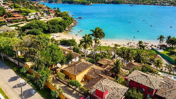 Un pueblo costero con una playa, casas de techos de teja terracota y un mar azul cristalino.