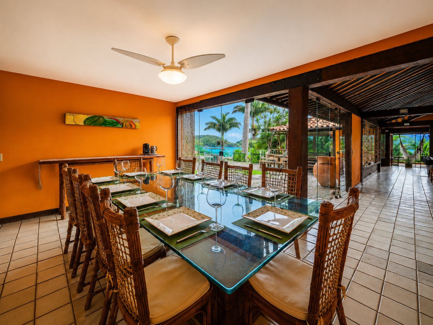 A dining area with a glass table, wicker chairs, and a view of the outdoors.