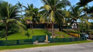 A tropical resort with palm trees, a paved pathway, and a building with a stone facade. - Bz81 Pé na areia na Praia da Ferradura (Buzios)