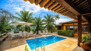 A pool area with a clear blue pool, white lounge chairs, and a wooden pergola. - Bz81 Pé na areia na Praia da Ferradura (Buzios)