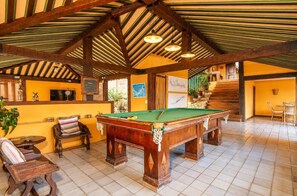 Une salle de billard équipée d’une table de billard, de meubles en bois et d’un escalier menant à un niveau supérieur.