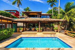 A pool area with a clear blue pool, wooden deck, and outdoor seating. - Bz81 Pé na areia na Praia da Ferradura (Buzios)