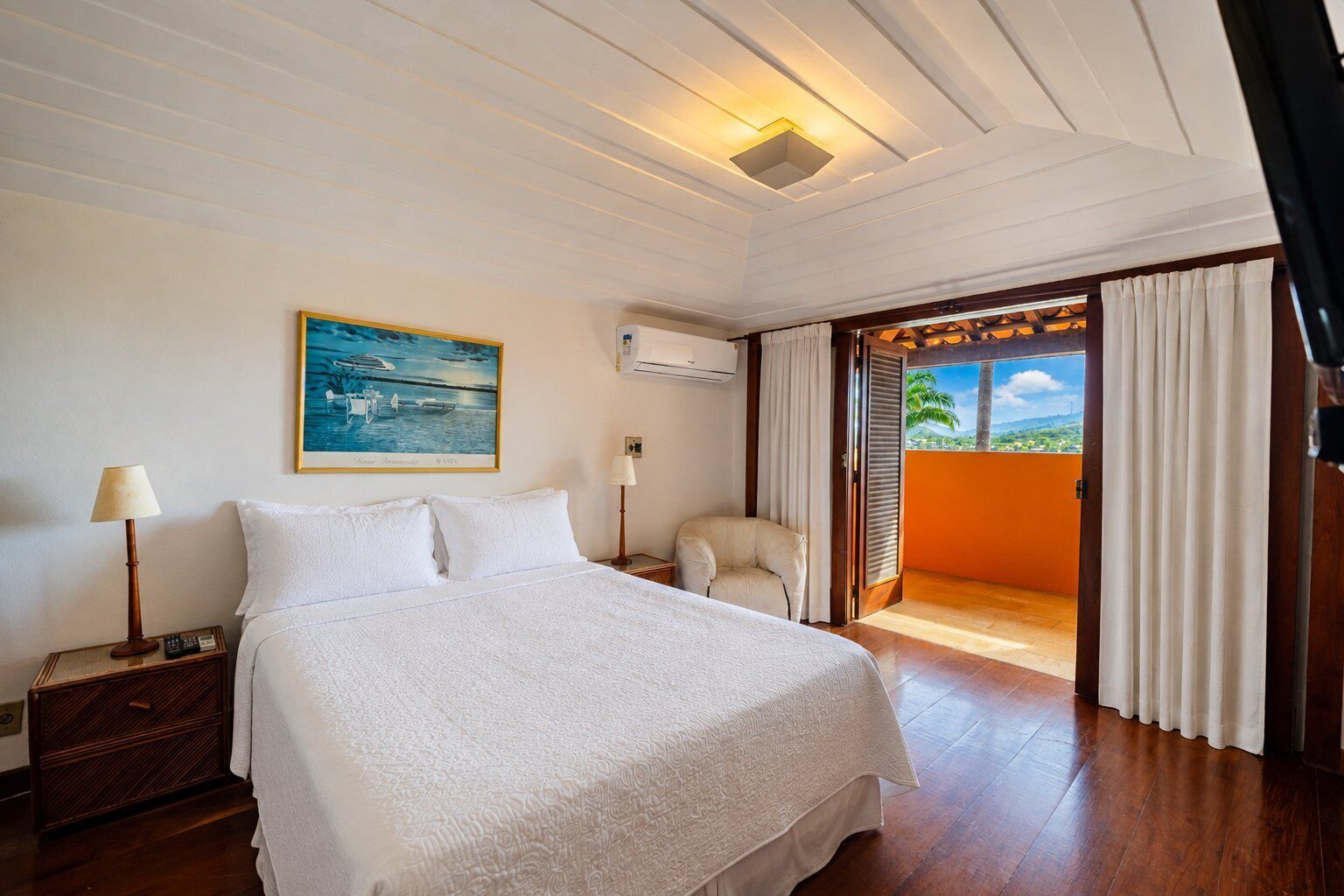 Habitación de hotel con cama, mesita de noche, una silla, unidad de aire acondicionado y un cuadro en la pared.