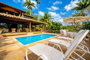 Un área de piscina con sillones reclinables y una zona de estar cubierta.