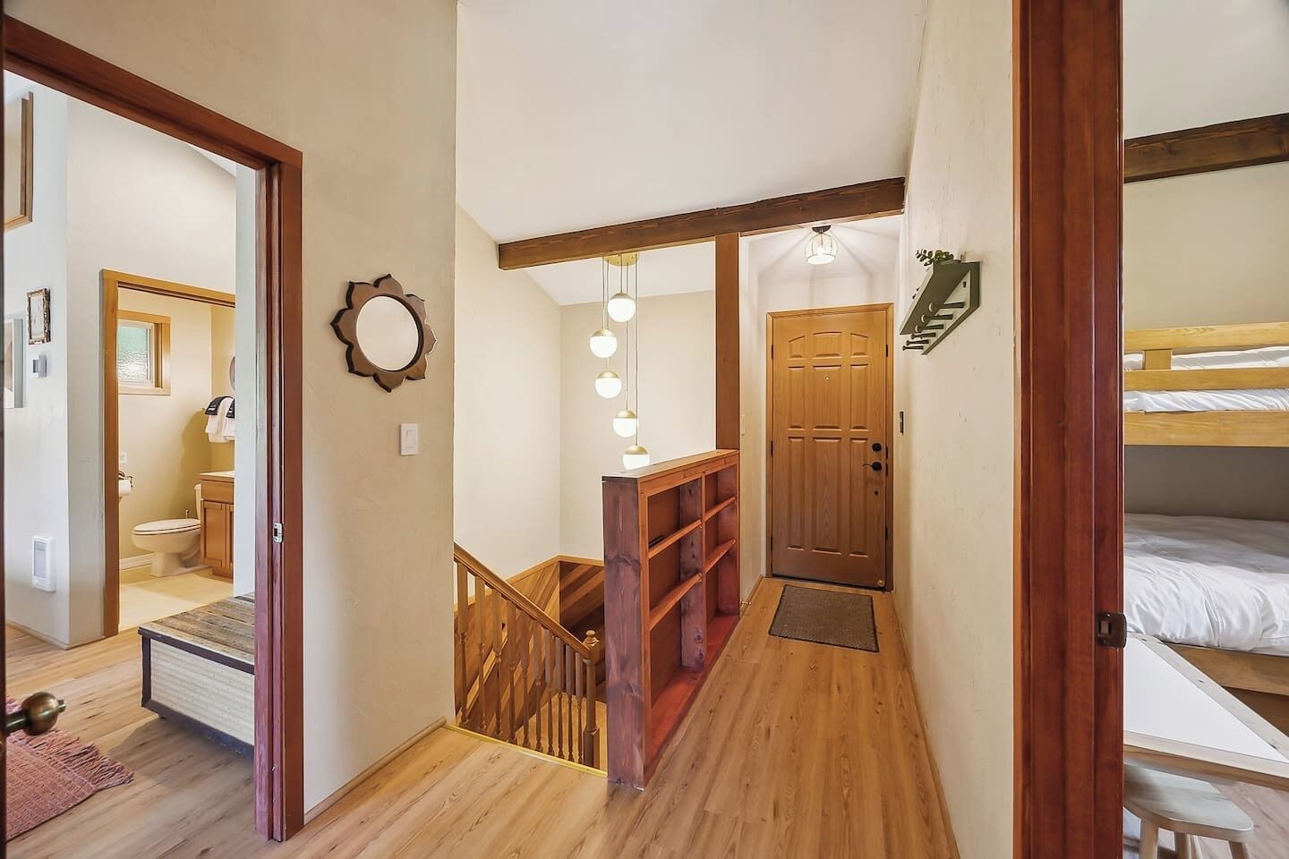 Un couloir étroit avec un plancher en bois, un escalier avec une rampe en bois, une porte avec une enseigne verte et, au fond, un lit superposé.