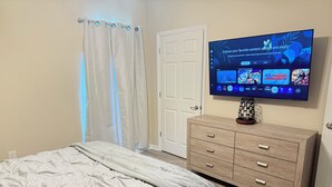 Ein Schlafzimmer mit einem Bett, einem an der Wand montierten Fernseher, einem Schminktisch und einer Tür.