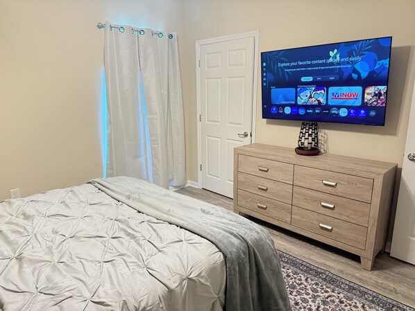 A bedroom with a bed, a TV mounted on the wall, a dresser, and a door.