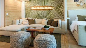 A cozy living room with a sofa, ottomans, a coffee table, and a wall with a palm leaf pattern. - City Skyline View Private Studio at Roney Palace (Miami Beach)