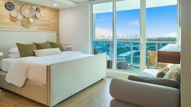 A modern bedroom with a large bed, a view of a cityscape through floor-to-ceiling windows, and a balcony with a table and chairs. - City Skyline View Private Studio at Roney Palace (Miami Beach)