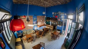 A restaurant with a blue interior, brick walls, wooden furniture, and hanging red lamps. - La Comunidad Hostel (Rosario)