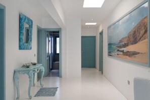 A hallway with a blue door, a wall-mounted mirror, and a painting of a beach scene.