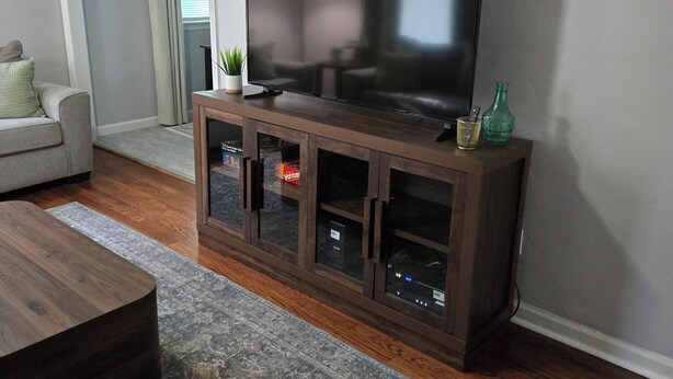 A living room with a flat-screen TV on a wooden cabinet, a gray sofa, a coffee table, and a patterned rug. - Midwest City 2 Bed 2 Bath-Cottage on 15th, Cottage on 15th-Charming  2 Bedroom (Midwest City)