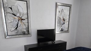 A bedroom with a bed, a dresser, a television, and two framed abstract paintings on the wall. - Midwest City 2 Bed 2 Bath-Cottage on 15th, Cottage on 15th-Charming  2 Bedroom (Midwest City)