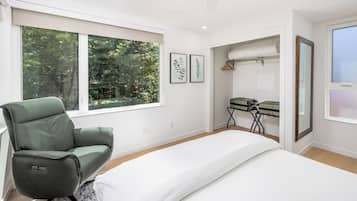Une chambre moderne avec un fauteuil vert, un lit, un bureau avec une chaise et une grande fenêtre donnant sur des arbres.