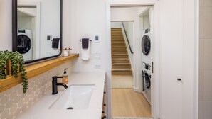 Un baño moderno con un lavamanos, un espejo y dos lavadoras al fondo.