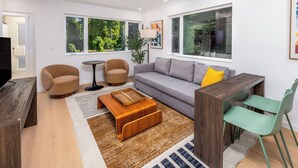 Una sala de estar moderna con un sofá, dos sillones, una mesa de centro, un televisor y un comedor con una mesa y sillas.