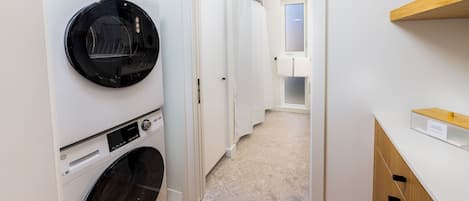 A laundry room with a front-loading washer and dryer, a wooden cabinet, and a shower area.