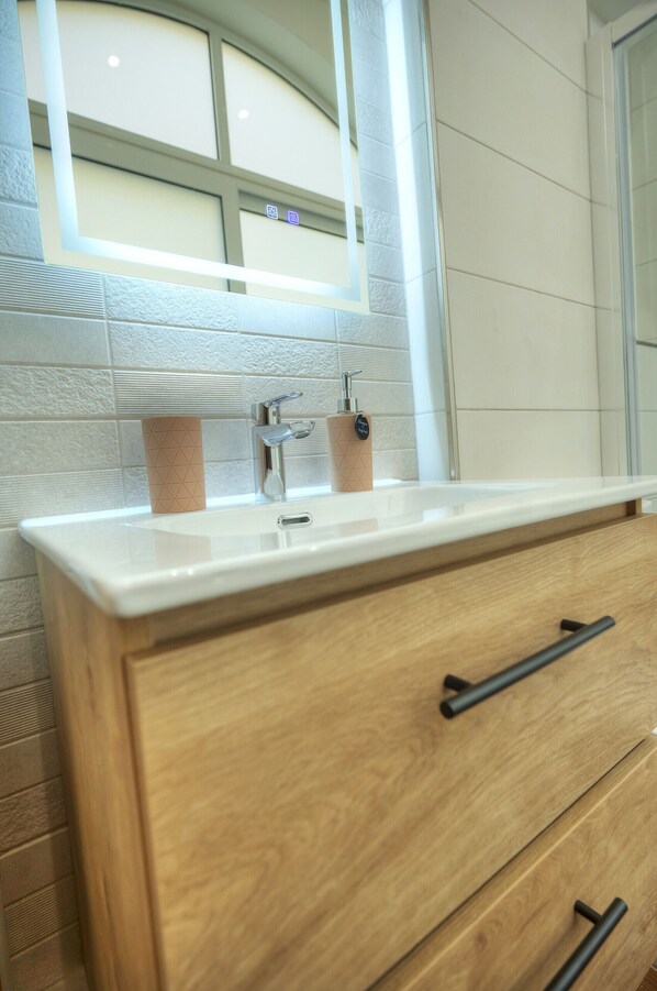 A bathroom with a white sink, wooden vanity, and a mirror with a window above it.