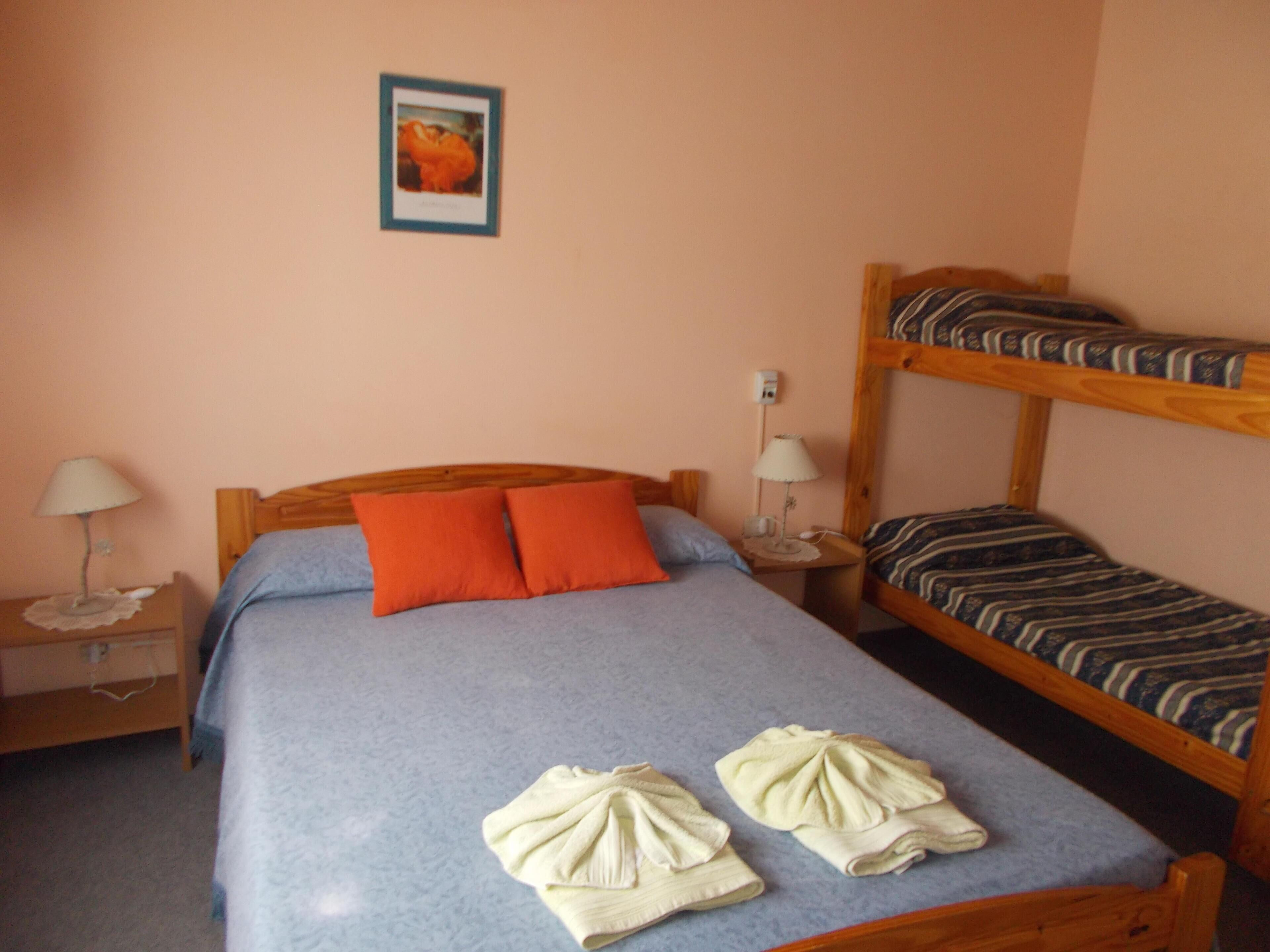 A bedroom with a single bed, two pillows, a nightstand with a lamp, a bunk bed, and a framed picture on the wall.