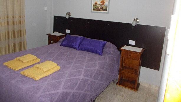 A bedroom with a bed, two nightstands, a headboard, a wall-mounted lamp, and a painting. - Hotel Brisas (San Clemente)