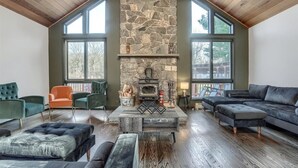 A spacious living room with a stone fireplace, large windows, and modern furniture. - 7BR Monroe Getaway: Pool, Hot Tub, & Huge Living Space (Monroe)