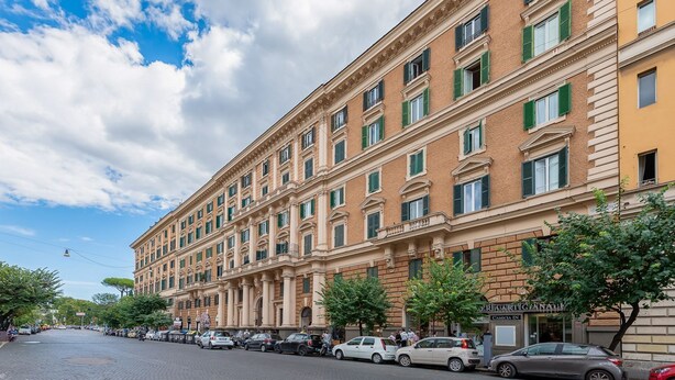 A multi-story hotel with a classical facade, large windows, and a tree-lined street.