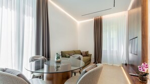 A modern living room with a glass coffee table, a sofa, and a TV mounted on the wall.