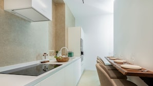 A modern kitchen with a central island, a dining area with a wooden table and chairs, and a built-in oven.