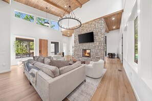 A spacious living room with a stone fireplace, a large sofa, and a flat-screen TV mounted on the wall.