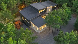 A modern two-story house surrounded by dense forest, featuring a large deck and a stone exterior.