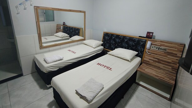 A hotel room with two beds, a mirror, an air conditioning unit, a wooden reception desk, and a telephone. - Hotel Flert Santana (Sao Paulo)