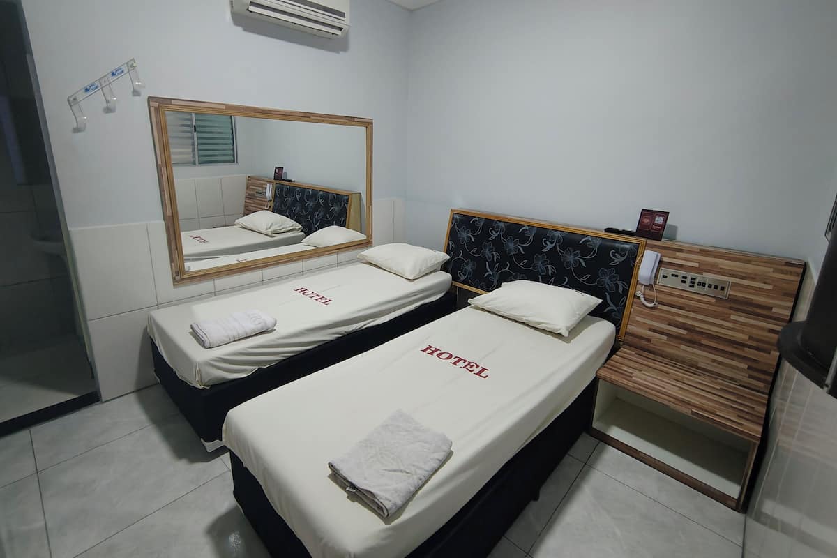 Een hotelkamer met twee bedden, een spiegel, een airconditioningapparaat, een houten receptiebalie en een telefoon.