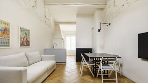A modern living room with a sofa, a dining table with chairs, a kitchen in the background, and a TV mounted on the wall. - Elegant Apartment in the Heart of Florence (Firenze)