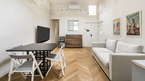 A compact living space with a dining area, a sofa, a TV, and a wooden herringbone floor. - Elegant Apartment in the Heart of Florence (Firenze)