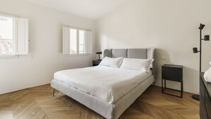 A modern bedroom with a large bed, a nightstand, a lamp, and a view of the outside. - Elegant Apartment in the Heart of Florence (Firenze)