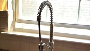 A kitchen sink with a flexible hose faucet, a granite countertop, and a window with blinds in the background. - Cozy 2-bedroom apartment with WiFi, AC, large outdoor balcony (Belleville)