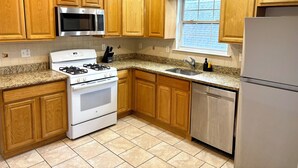 A kitchen with wooden cabinets, a stainless steel refrigerator, a microwave, a stove, and a dishwasher. - Cozy 2-bedroom apartment with WiFi, AC, large outdoor balcony (Belleville)
