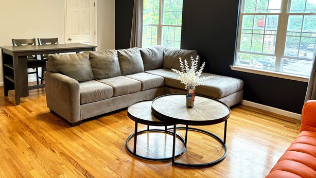 A living room with a gray sectional sofa, a round coffee table, and a dining table with chairs. - Cozy 2-bedroom apartment with WiFi, AC, large outdoor balcony (Belleville)