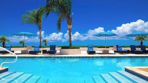 A clear blue pool with lounge chairs and umbrellas, surrounded by palm trees and a clear sky. - Hidden Haven III - Cozy Studio (The Bight Settlement)