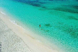 Een strand met helder turquoise water en een persoon in het water staand.