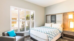 A hotel room with a bed, a chair, a nightstand, and a window with blinds. - Hidden Haven III - Cozy Studio (The Bight Settlement)