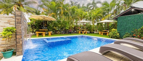 A swimming pool with lounge chairs, a stone wall, and lush greenery.
