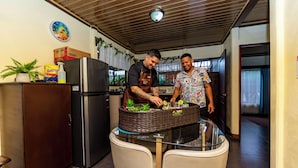Een keuken met een koelkast, een eettafel met stoelen en een klok aan de muur.