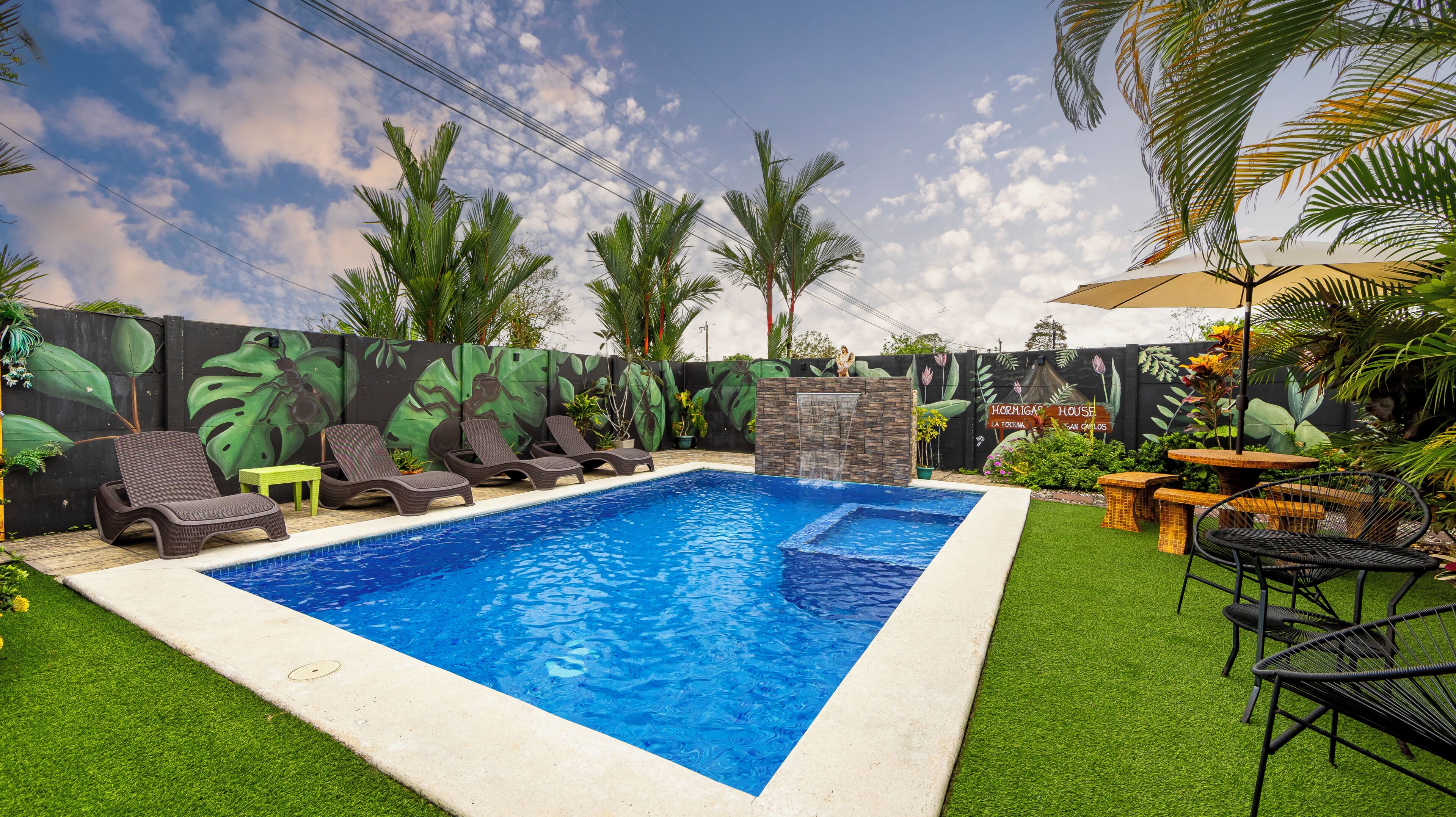 Une piscine entourée de chaises longues, d’un mur en pierre et de plantes tropicales.