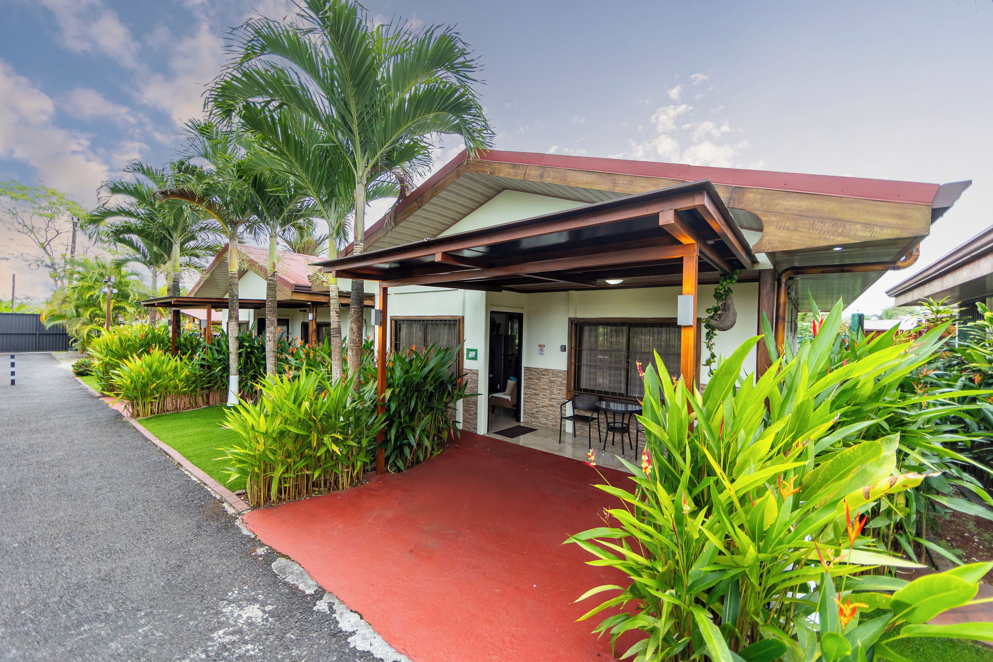 A building with a covered entrance, a red pathway, and lush greenery.