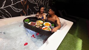Een hottub met een mand vol eten en drinken, omringd door een muur met een bladmotief.