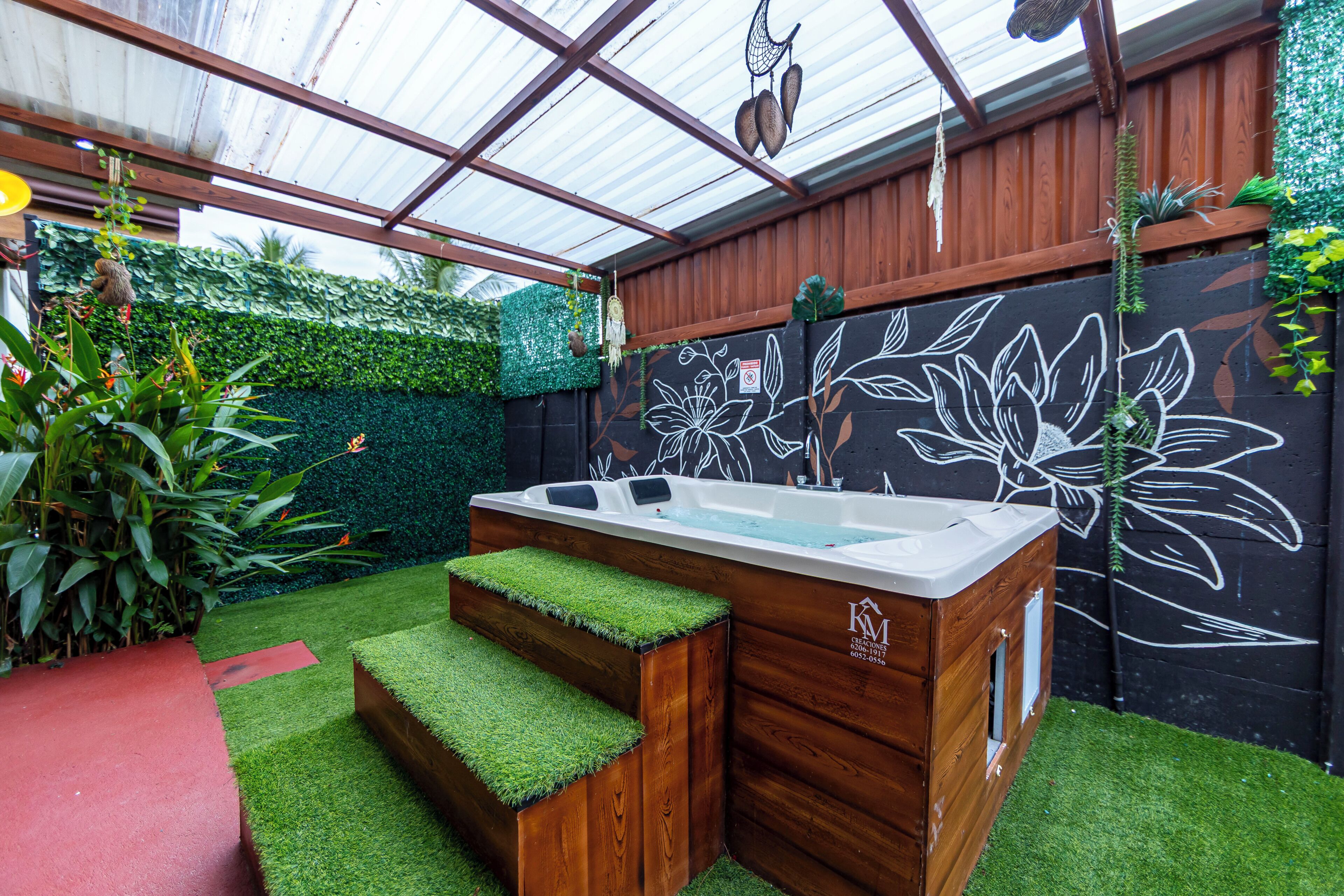Un jacuzzi con escalones, rodeado por una terraza de madera y una pared verde con un mural floral.